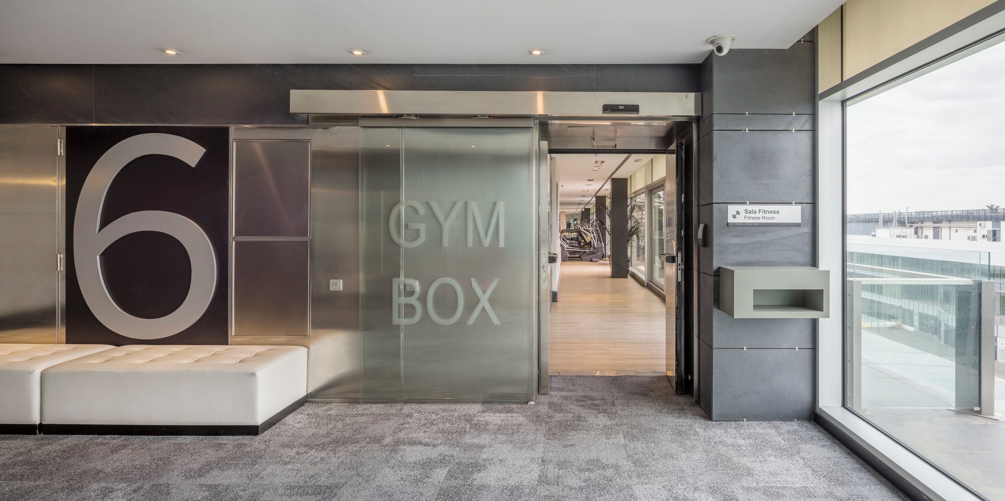 En moderne hotellobby med et stort skilt med '6', et skilt med 'GYM BOX' og et skilt med 'Fitnessrum'.