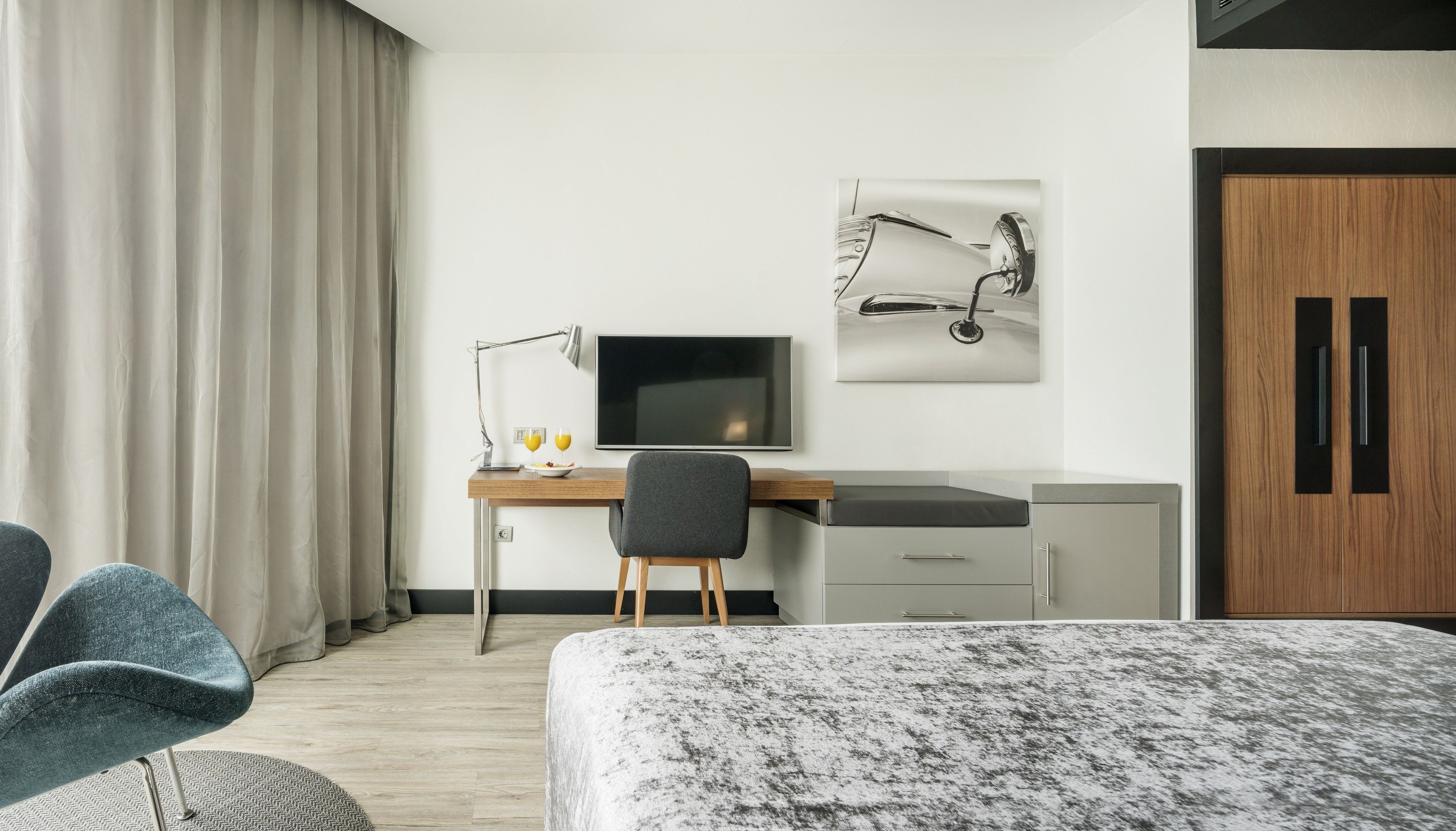 Una habitación de hotel moderna con una cama, un escritorio con ordenador, una silla, un televisor y un armario.