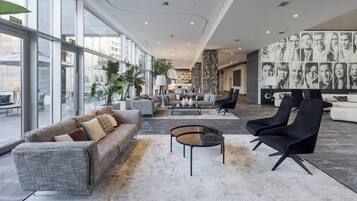 Eine großzügige Hotelhalle mit modernem Design, ausgestattet mit einer breiten Sitzecke, Sofas und Sesseln, einem zentralen Couchtisch und einer Wand mit Porträts.