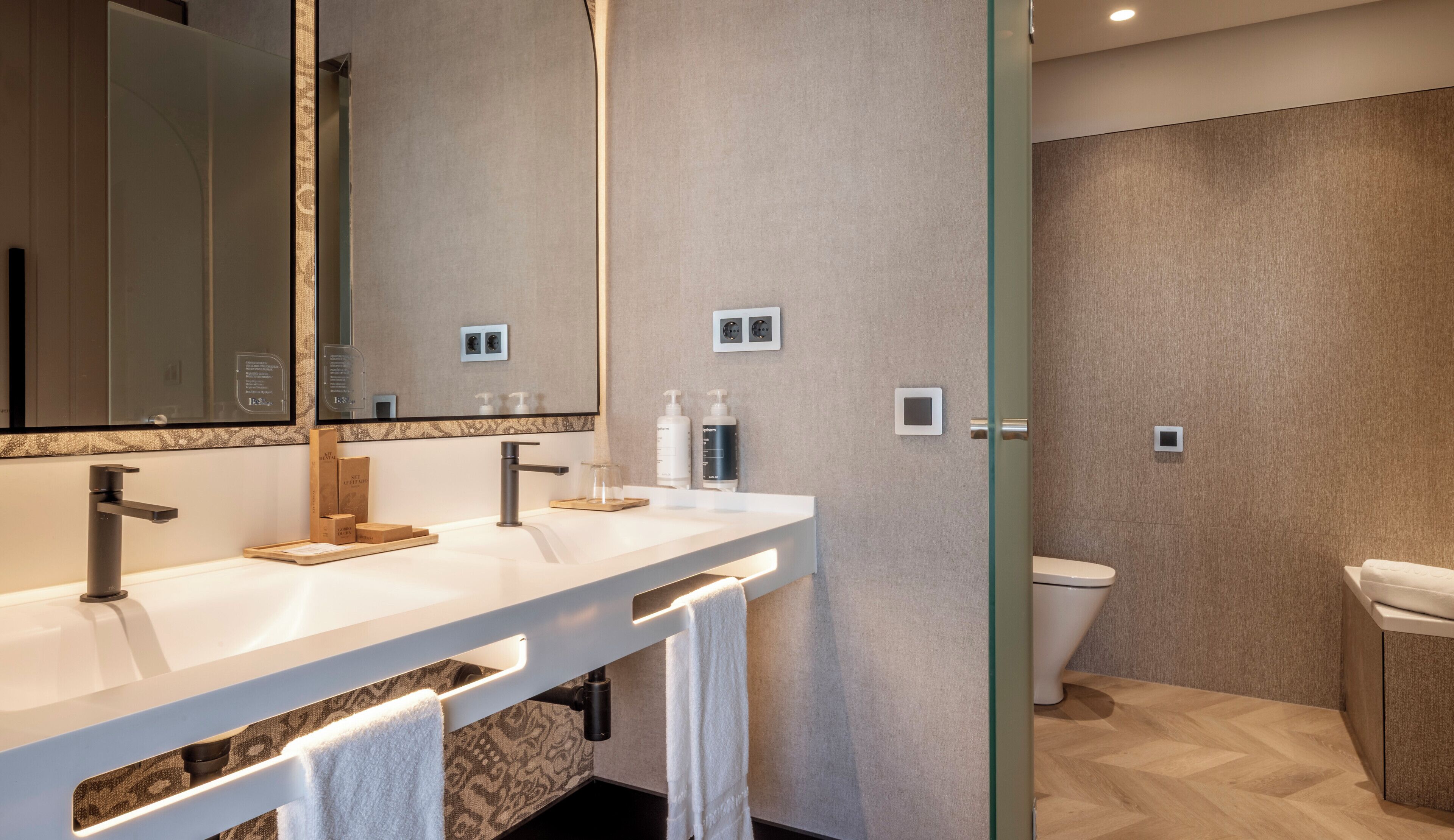 Een moderne badkamer met een grote spiegel, twee wasbakken, een toilet en een douchehoek.