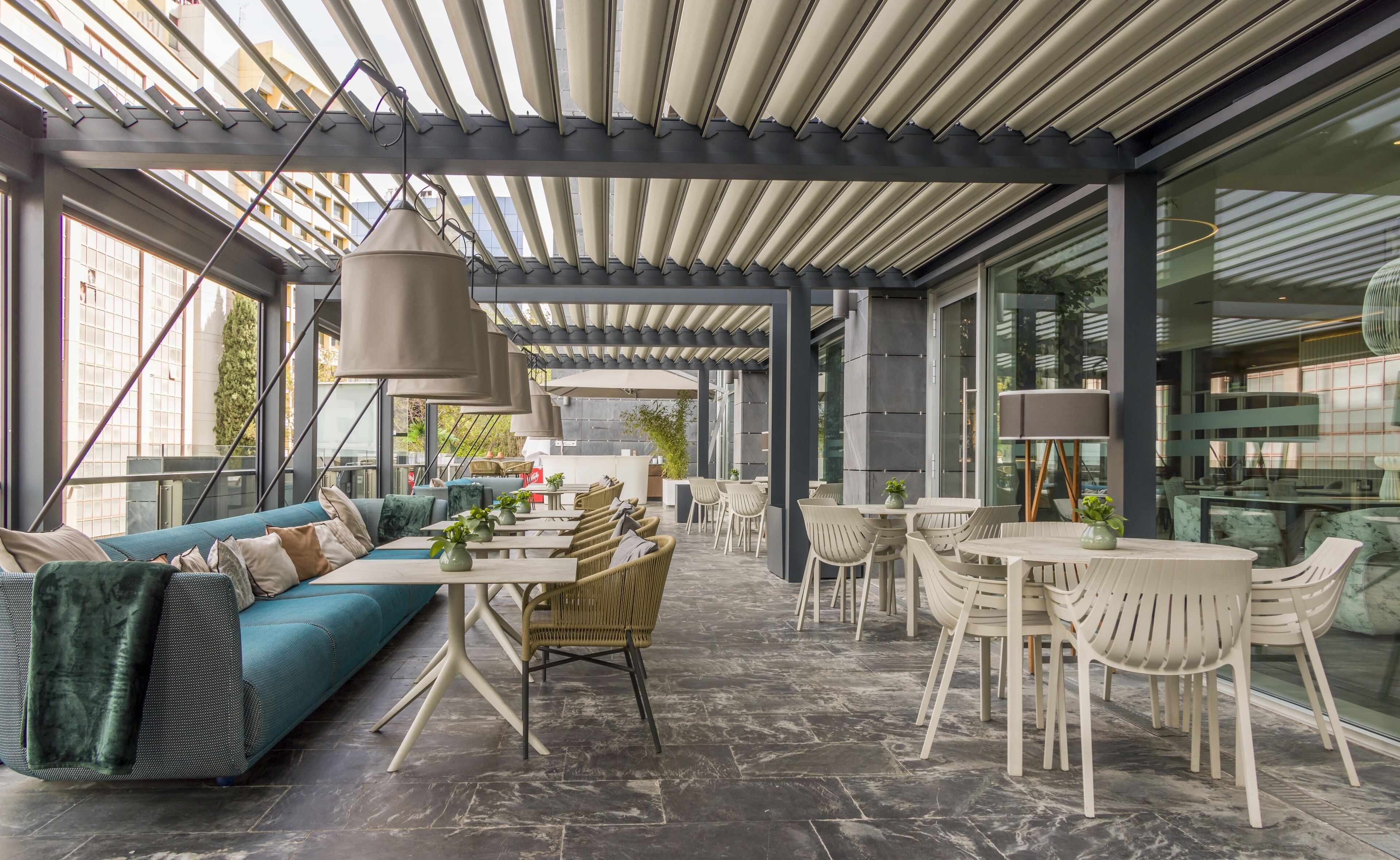 Ein moderner Essbereich im Freien mit verschiedenen Sitzmöglichkeiten, darunter eine Sitzecke und Tische, unter einer überdachten Pergola.