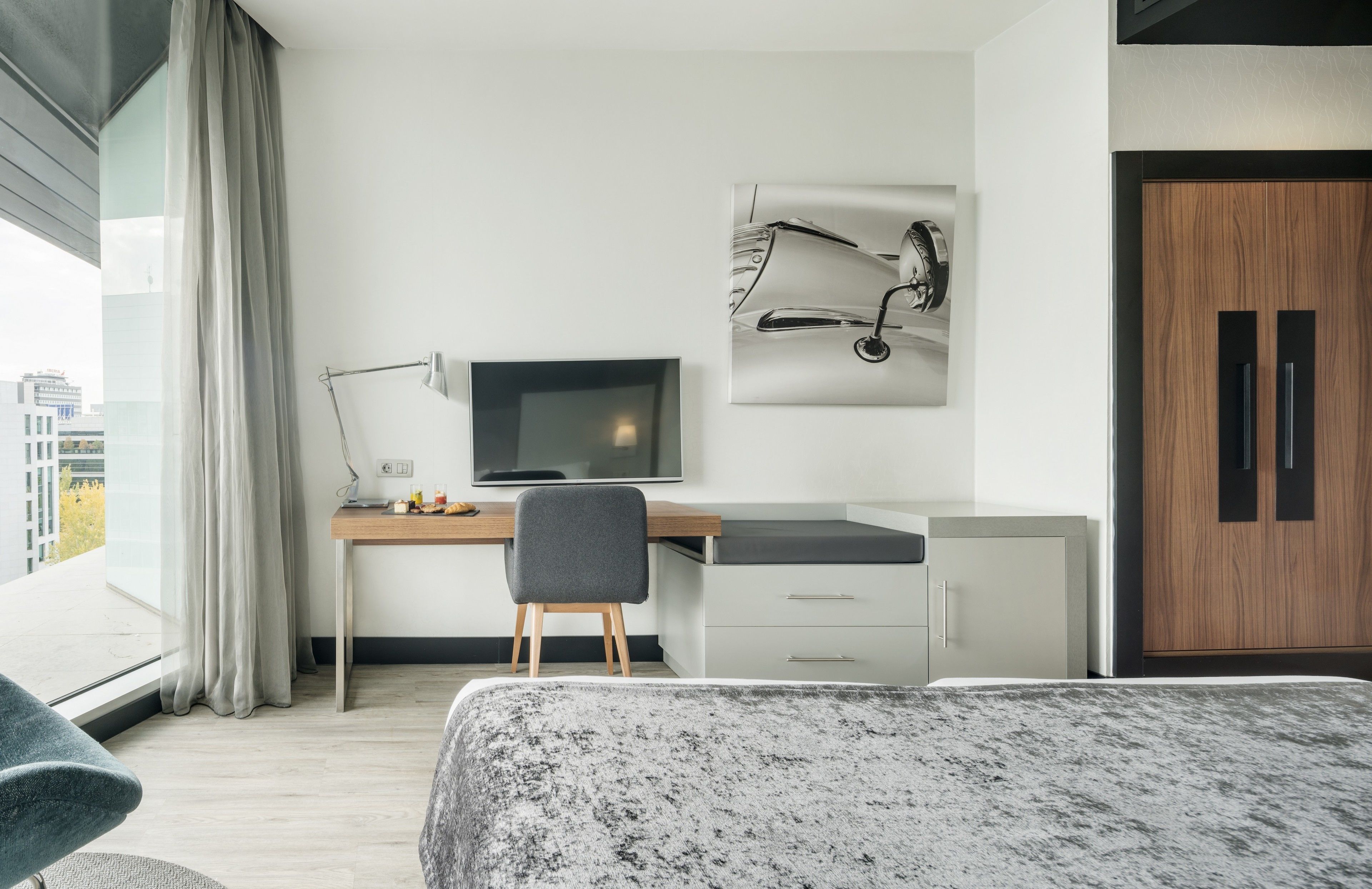 Una habitación de hotel moderna con una cama grande, un escritorio con una computadora, una silla y un armario.
