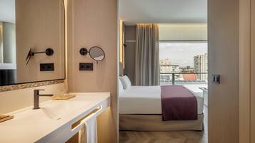 A hotel room with a modern bathroom, a bed with a view, and a cityscape visible through the window.