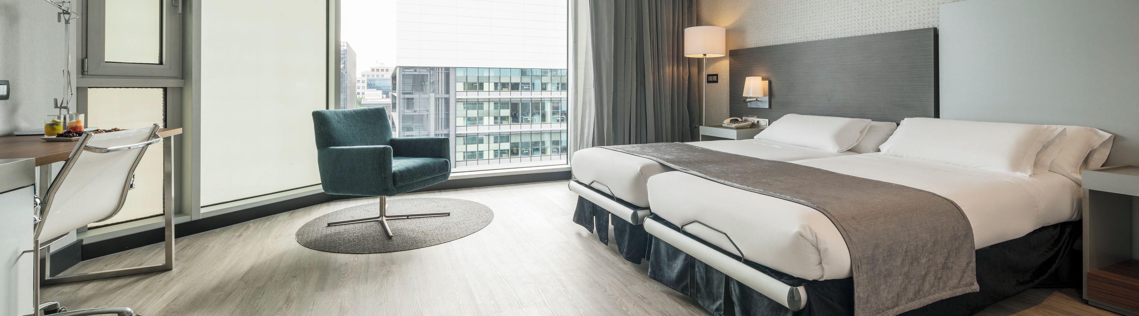 Ett hotellrum med en säng, ett skrivbord, en stol, ett nattduksbord och ett fönster med utsikt över staden.