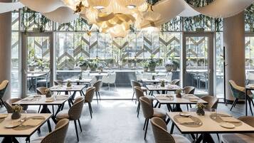 Ein modernes Restaurant mit einer zentralen Sitzgruppe, großen Fenstern und hängenden Pflanzen.