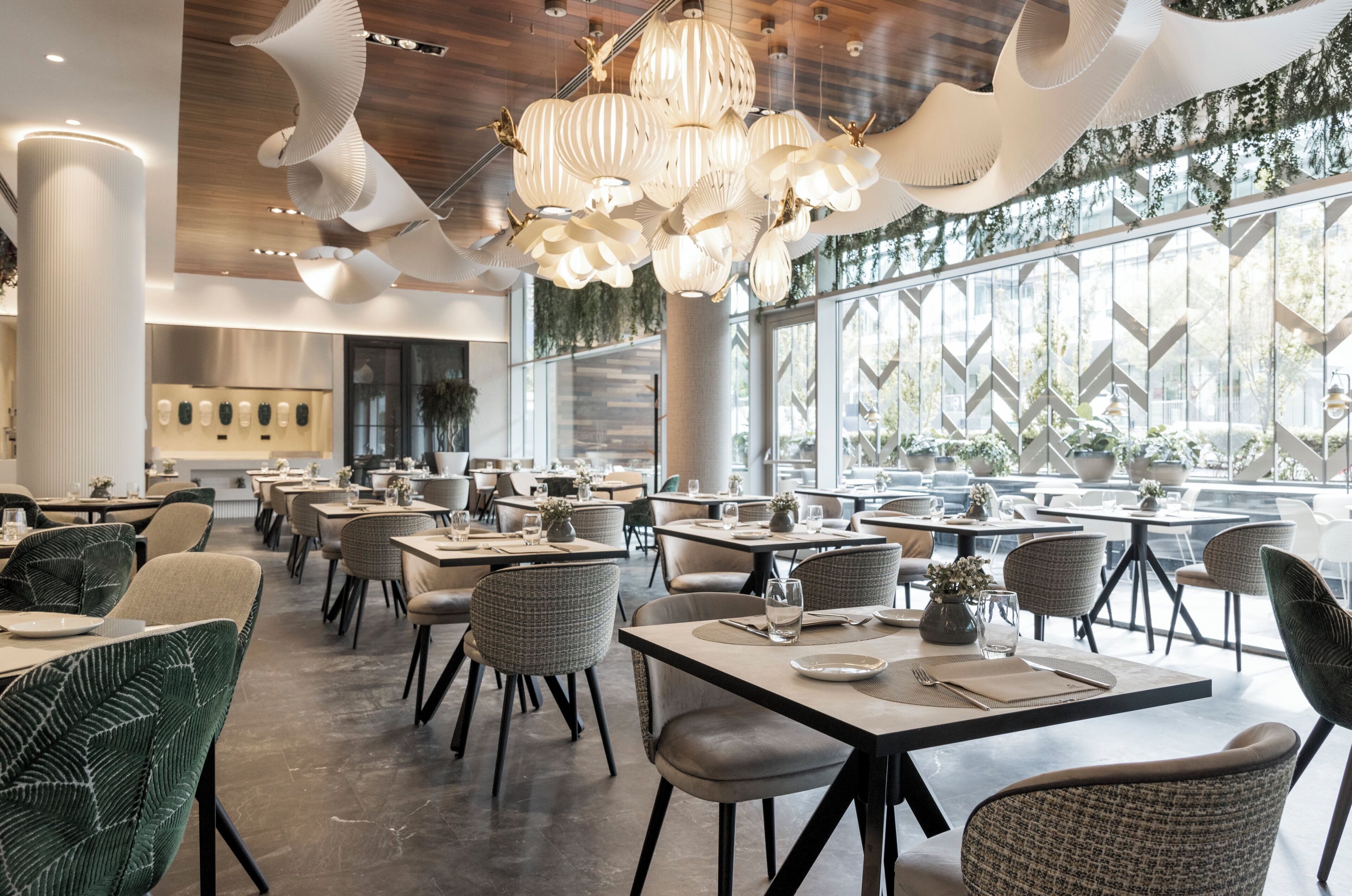 Un interior de restaurante moderno con techos altos, luces de techo originales y grandes ventanales con vegetación.