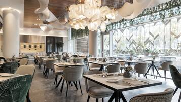 Un interior de restaurante moderno con techos altos, luces de techo originales y grandes ventanales con vegetación.
