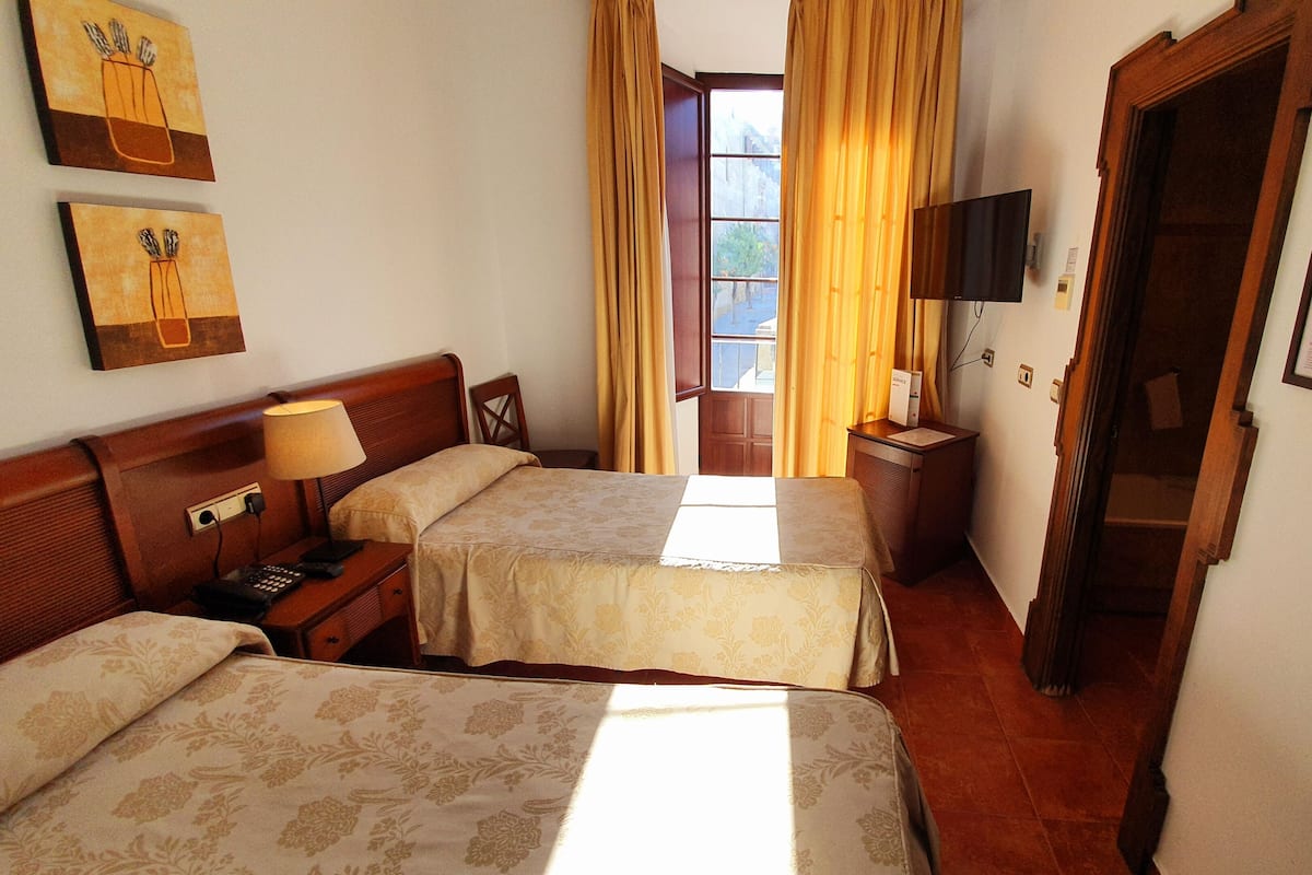Habitación de hotel con dos camas, un escritorio con lámpara, televisión y ventana con cortinas.