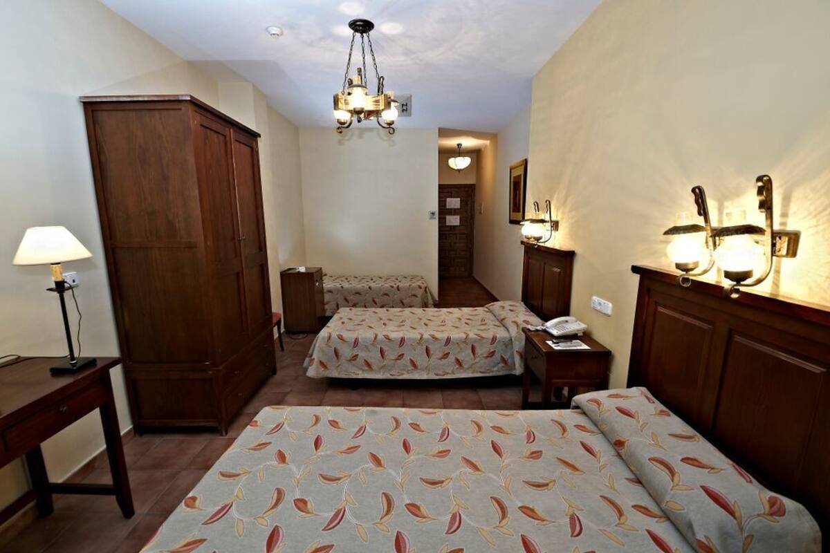 Habitación de hotel con dos camas, un armario de madera, un escritorio con lámpara y un candelabro.