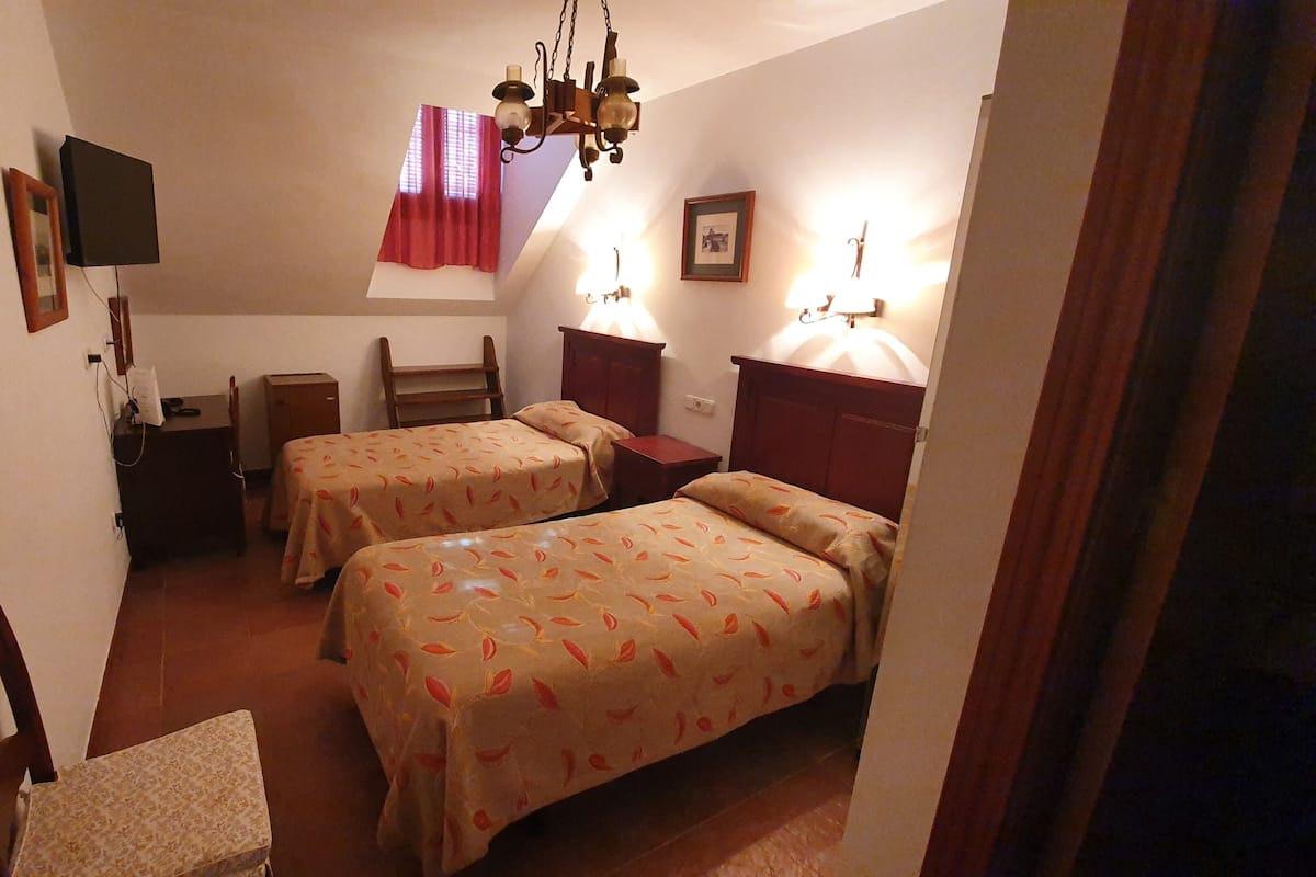 Una habitación pequeña y acogedora con dos camas individuales, un escritorio, una silla y un televisor.