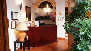 A reception area with a wooden reception desk, a lamp, and a sign indicating a reception. - Hotel Coso Viejo (Antequera)