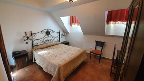 A bedroom with a bed, a chair, a nightstand, a lamp, and a window with curtains.