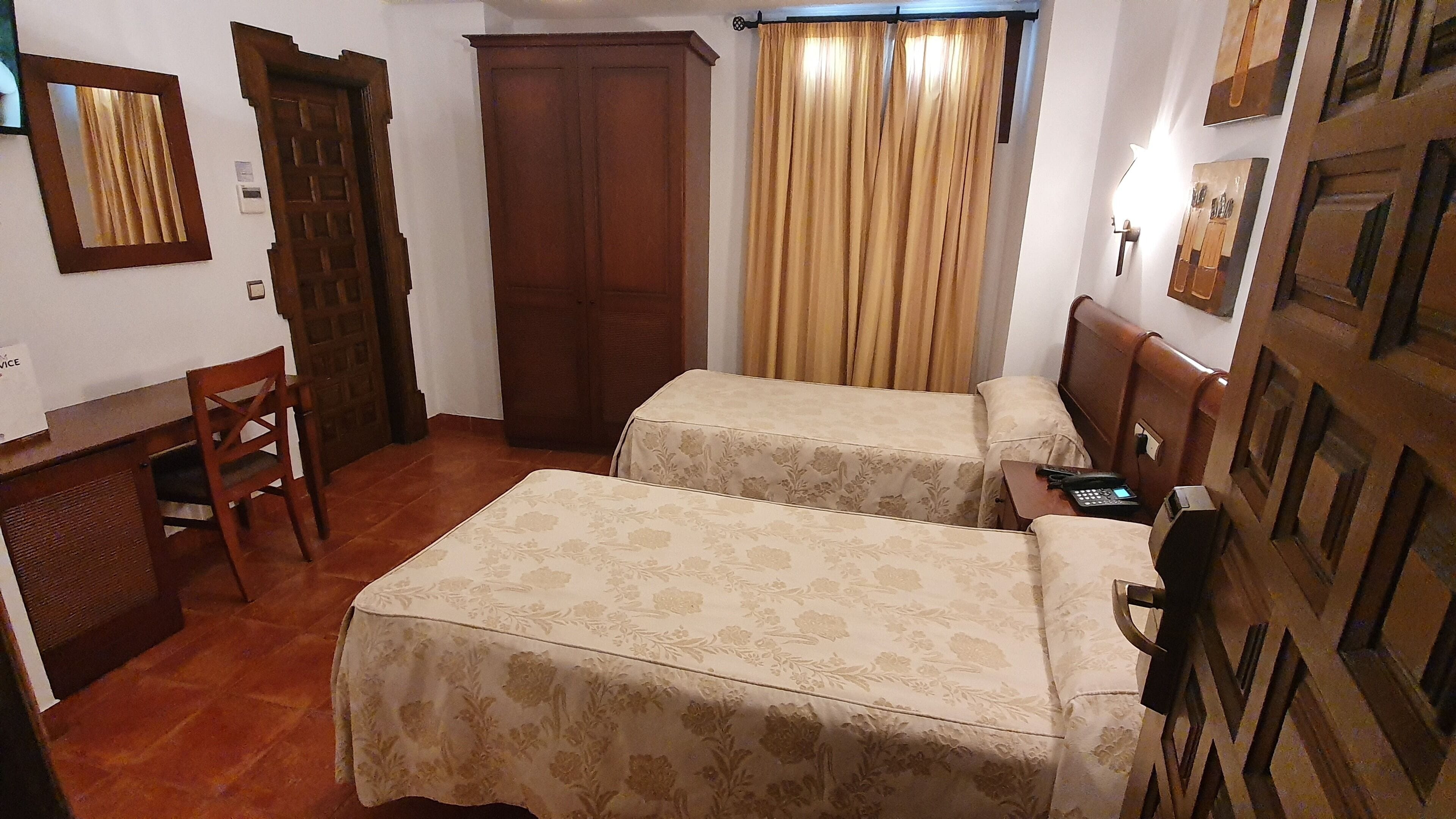 A room with two beds, a desk, a chair, a wardrobe, and a curtain.