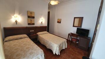 Habitación de hotel con dos camas individuales, un escritorio con silla, televisor e iluminación en la pared.