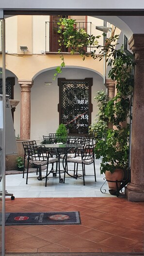 Un espace extérieur aménagé pour les repas, avec une table et des chaises, entouré de plantes en pot et agrémenté d’une grille décorative en métal.