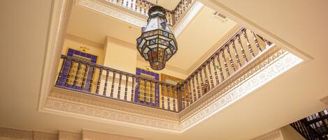 Interior de varios niveles con barandillas ornamentales, un farol colgante y obras de arte enmarcadas en las paredes.