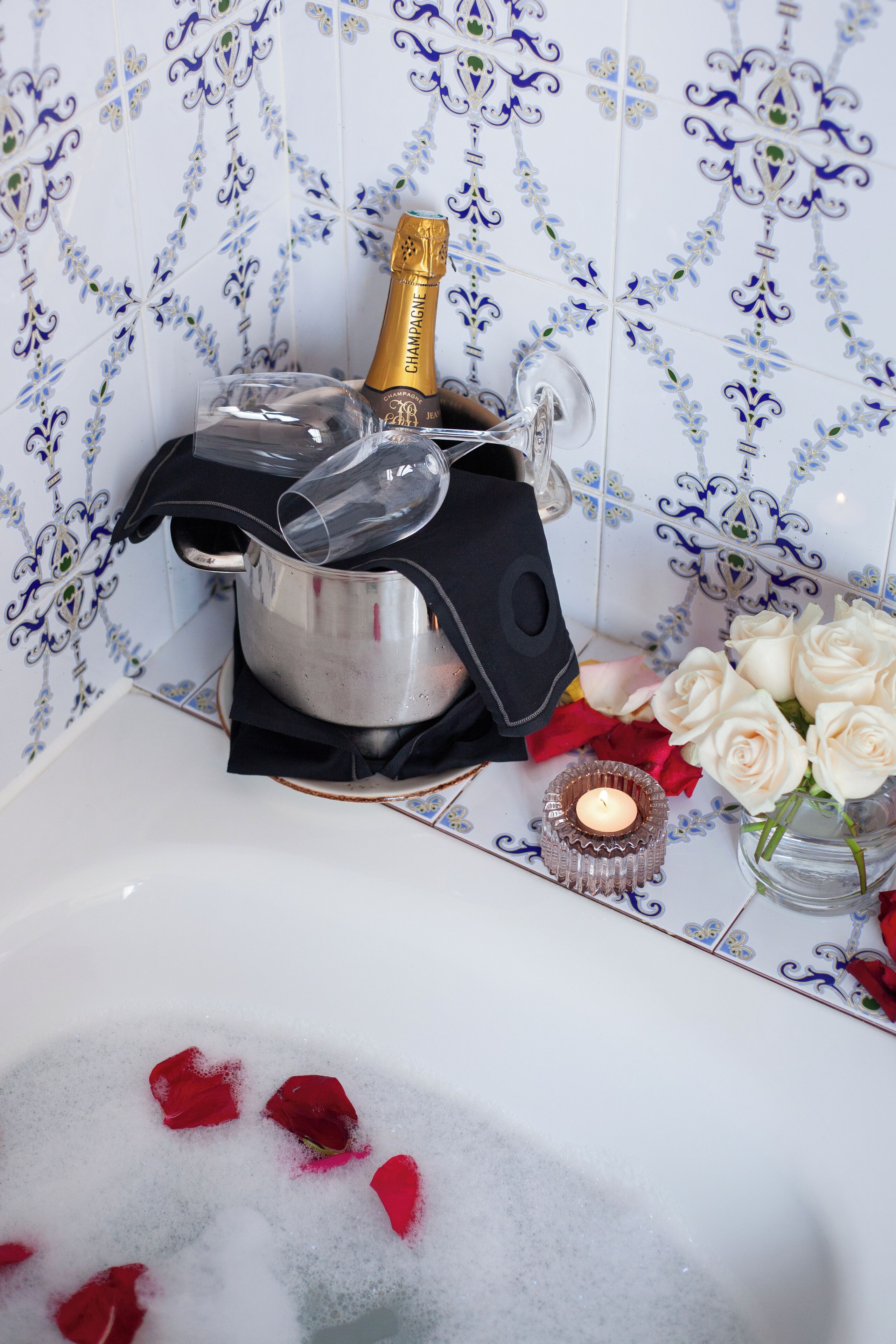 A bathtub with a champagne bottle, rose petals, and a candle.