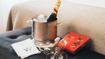 A metal bucket with a bottle of champagne, a box of chocolates, and two wine glasses on a dark surface.