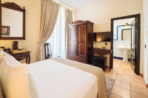 A hotel room with a large bed, a wardrobe, a desk with a chair, a television, and a bathroom with a mirror and sink. - Hotel Palacio de Hemingway (Ronda)