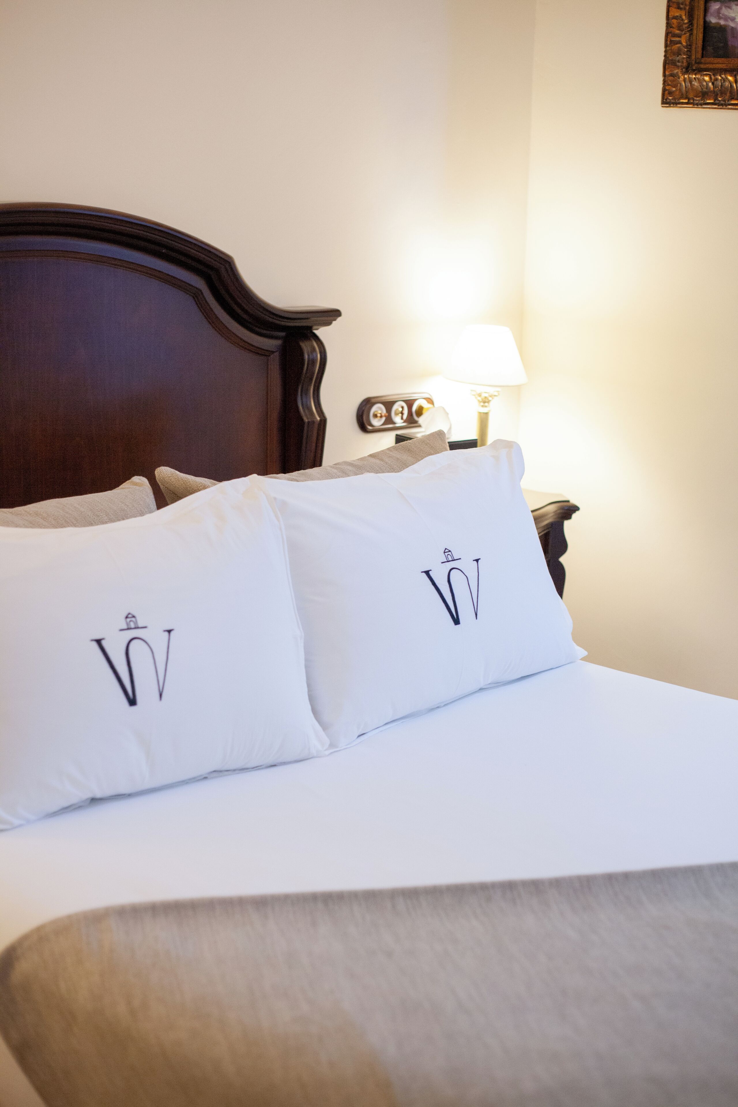 Una cama bien hecha con ropa blanca y dos almohadas con un diseño de monograma.