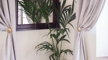 A room with a wooden chair, a potted plant, a mirror, and a window with curtains.