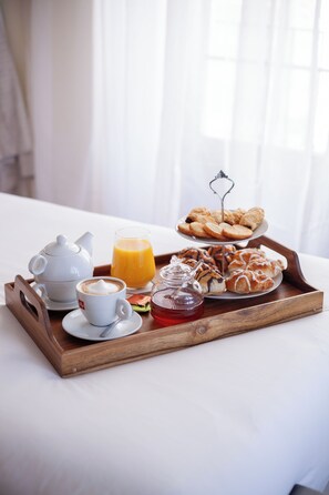 Un plateau de petit-déjeuner avec une théière, une tasse de café, du jus d’orange, des viennoiseries et un pot de miel, le tout posé sur un plateau en bois.