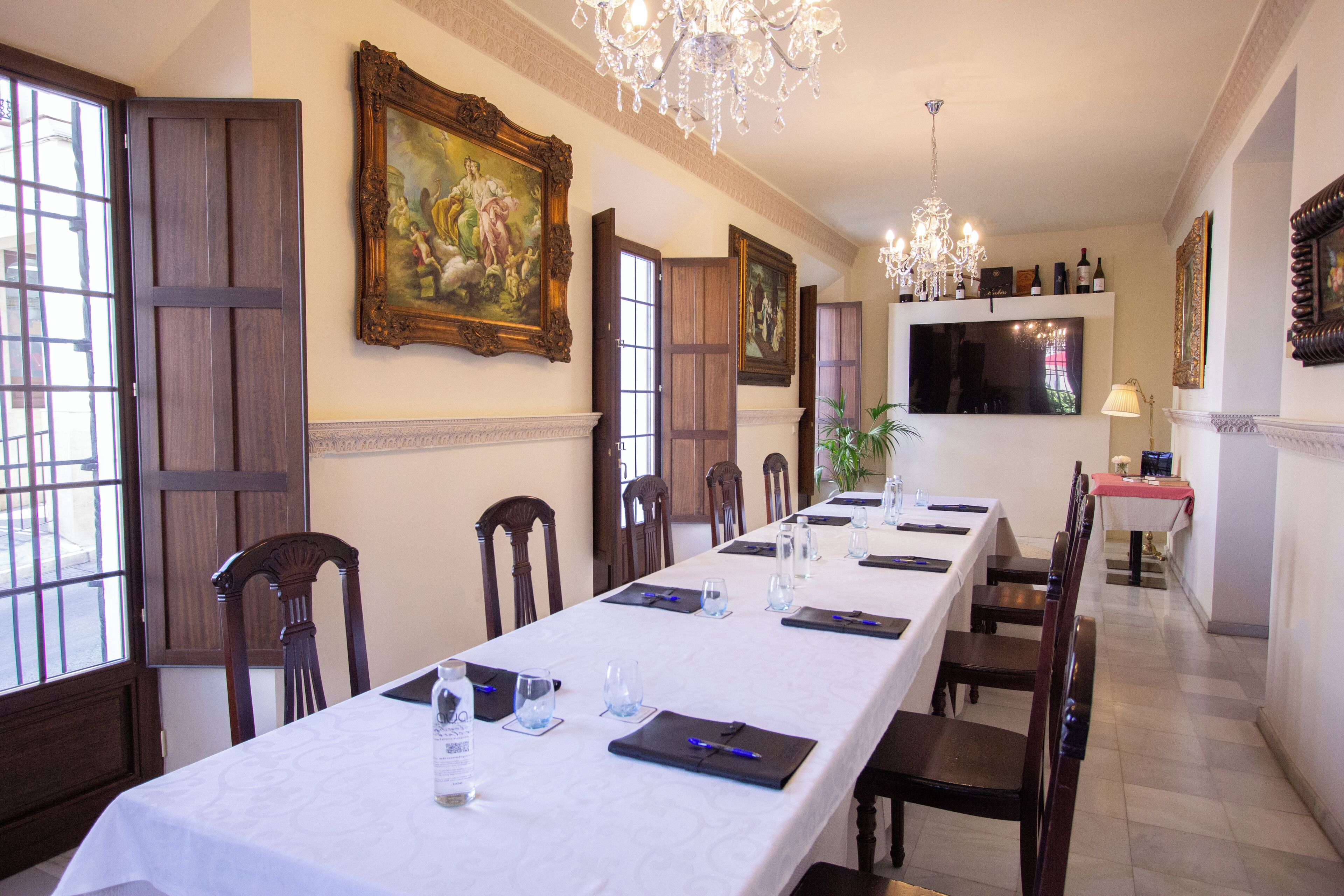 A dining room with a long table set for a meal, wooden chairs, a chandelier, and framed artwork on the walls.