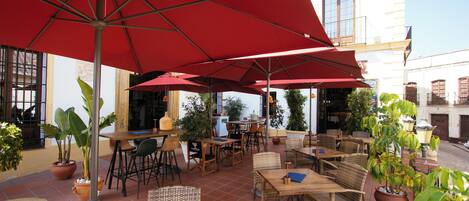 An outdoor patio with red umbrellas, wicker furniture, and potted plants.