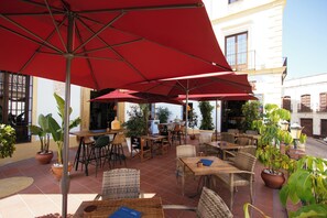 An outdoor patio with red umbrellas, wicker furniture, and potted plants. - Hotel Palacio de Hemingway (Ronda)