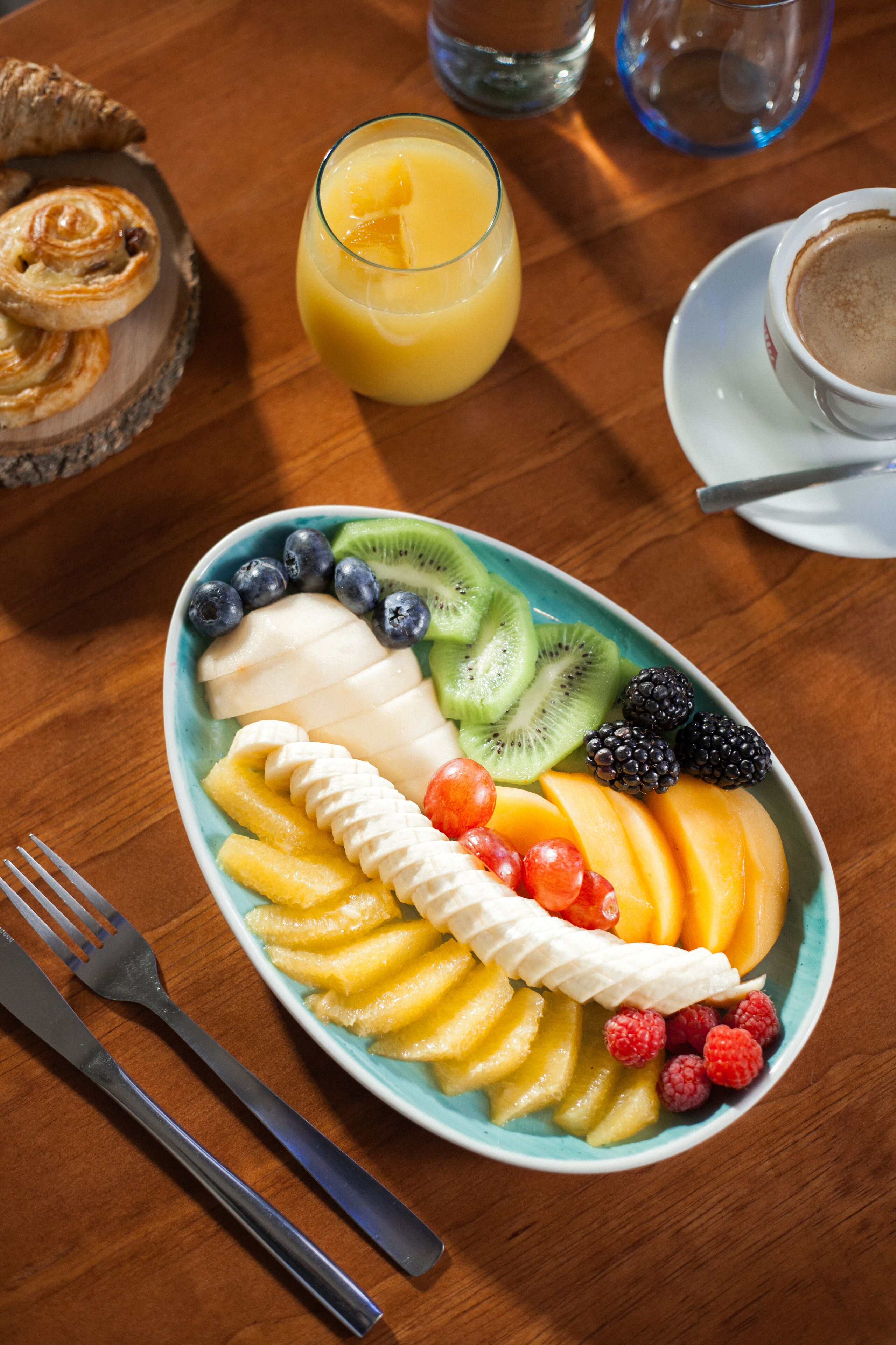 A breakfast plate with various fruits, a glass of orange juice, and a cup of coffee on a wooden table.