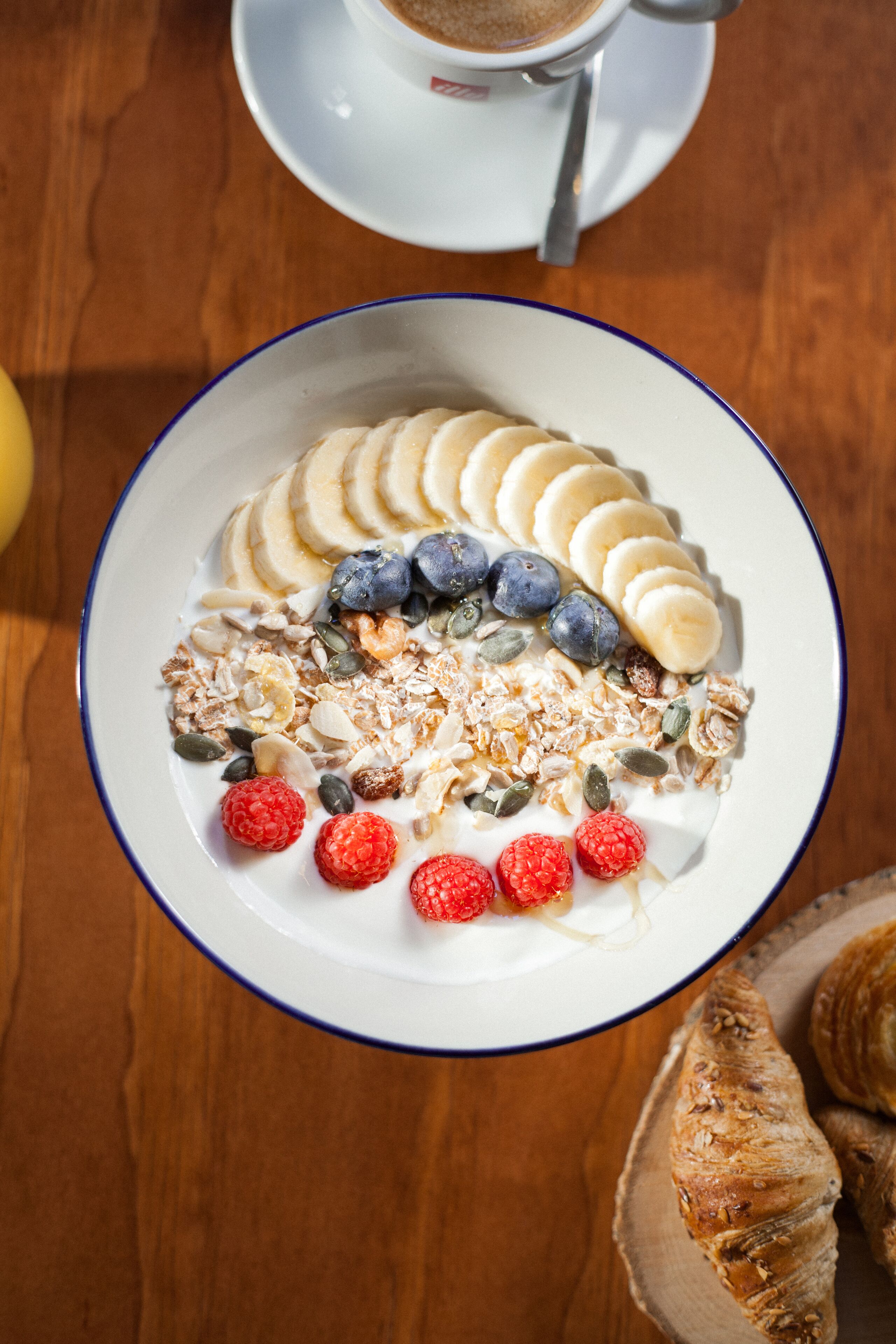 A bowl of cereal with fruits and granola on a wooden table.