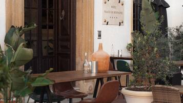 Un área de café al aire libre con mesas y sillas de madera, plantas en macetas y un letrero que indica que es el Hotel Palacio de Hemingway.