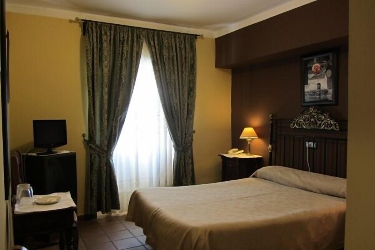 A hotel room with a bed, a desk with a lamp, a telephone, and a television.