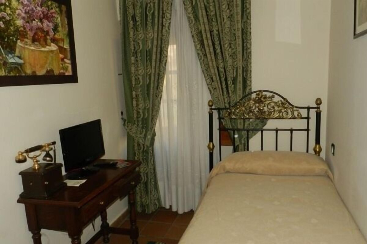 A bedroom with a bed, a desk with a computer, and a painting on the wall.