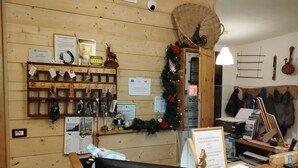 A wooden reception desk with a black chair, a key rack, a sign for the Albergo Sassi Rossi, a Christmas wreath, and a wall-mounted coat rack with jackets. - Hotel Ristorante Sassi Rossi  (Crandola Valsassina)