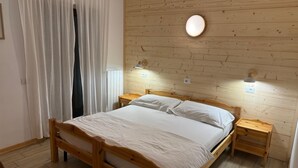 A wooden bed with white bedding, two bedside tables, a wall-mounted light, and a window with curtains. - Hotel Ristorante Sassi Rossi  (Crandola Valsassina)