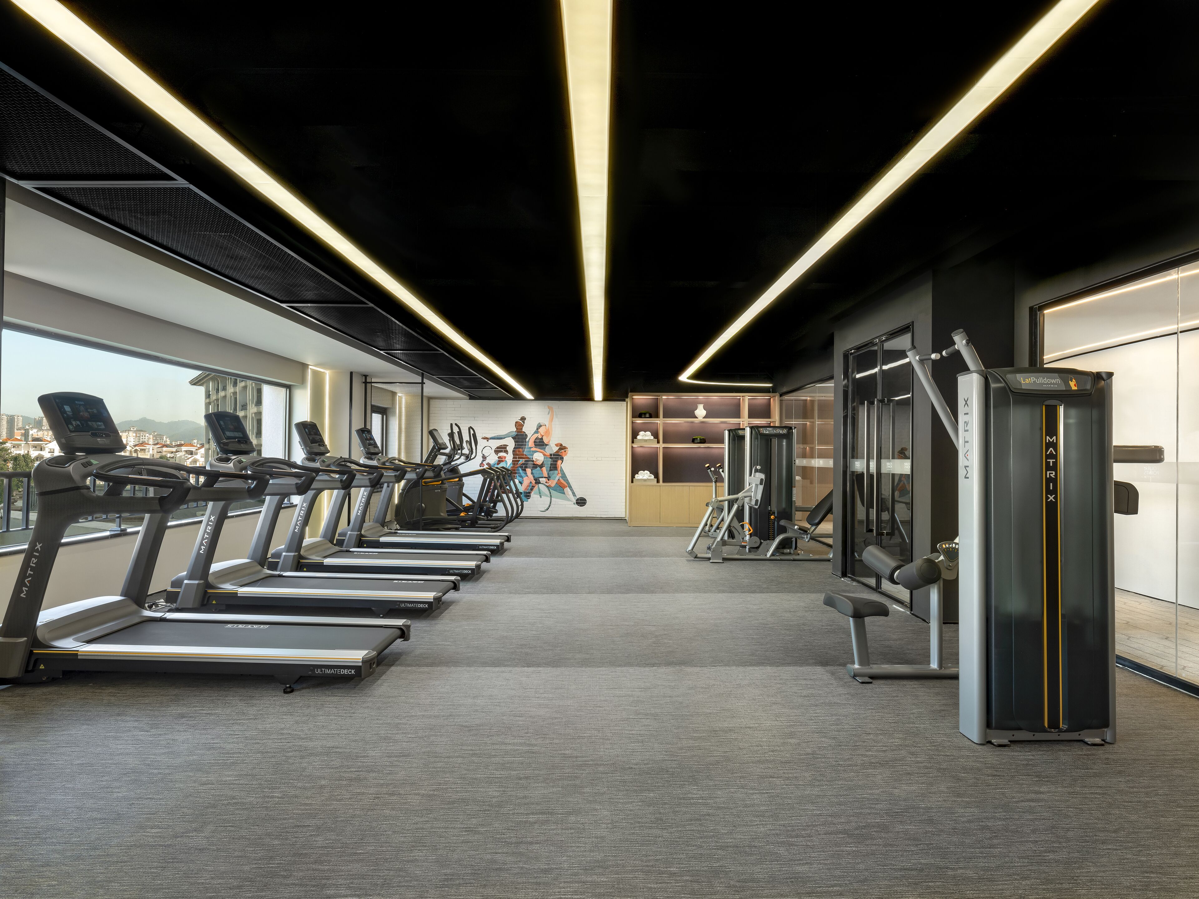 A gym with treadmills, a weight machine, and a mural on the wall.