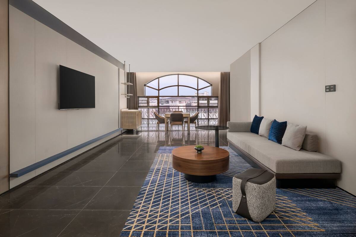 Une chambre d’hôtel moderne dotée d’une grande fenêtre, d’un téléviseur à écran plat, d’un canapé, d’une table basse et d’un tapis à motifs.