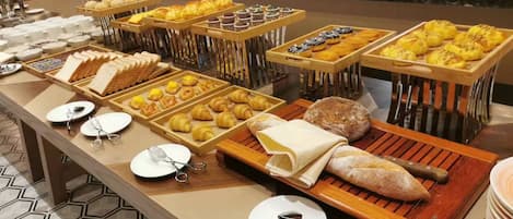 Un bufé con diferentes opciones de comida, incluyendo pan, pastelería y panes.
