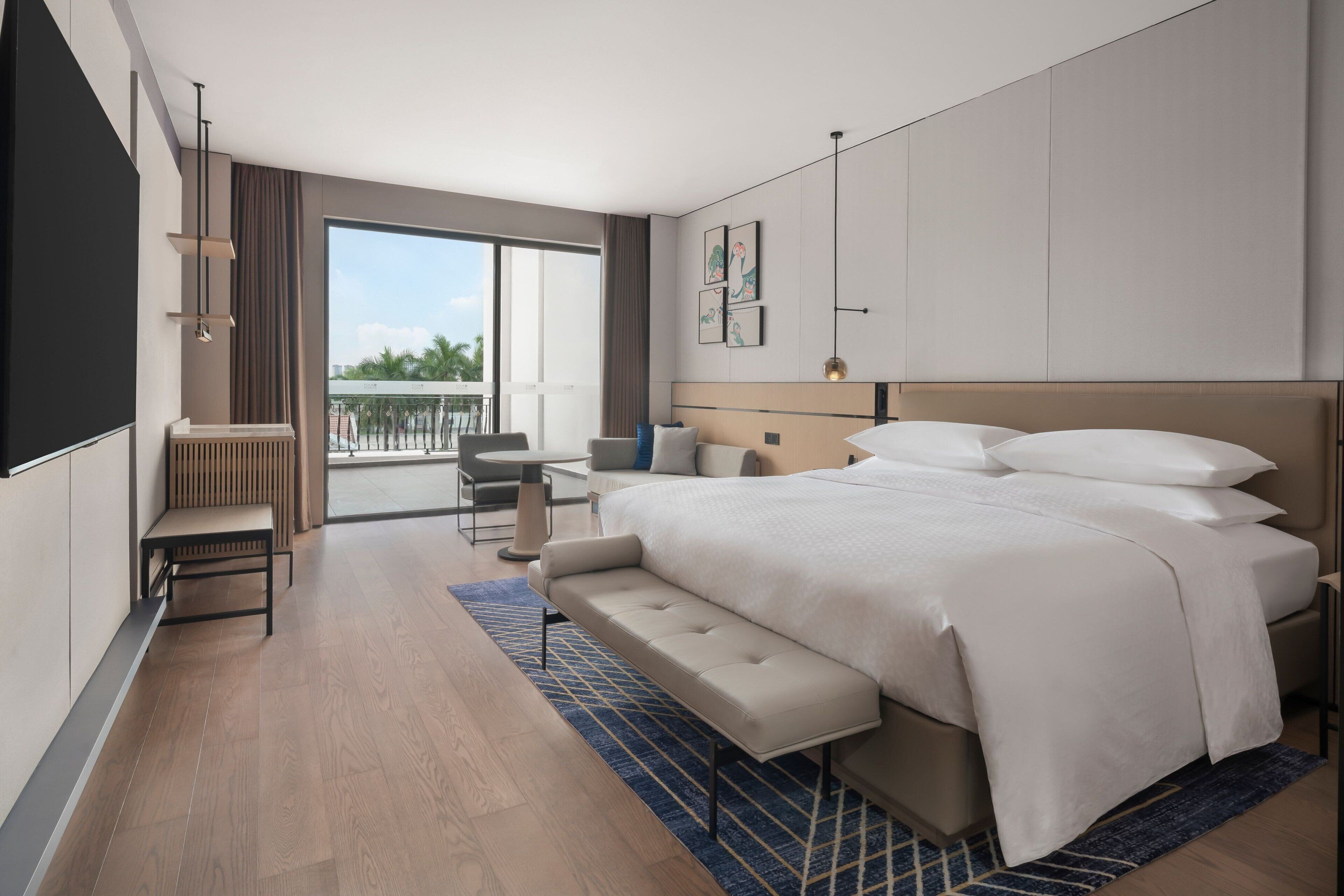 Ein modernes Hotelzimmer mit einem großen Bett, einer Sitzecke, einem Balkon und Blick ins Freie.