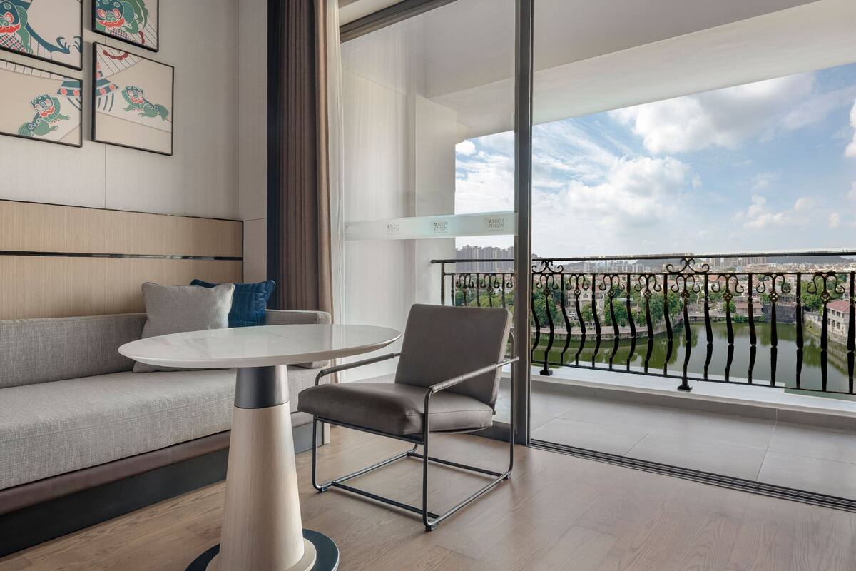 Un salon moderne avec un canapé, une table et une chaise. Il y a un balcon avec vue sur la ville.