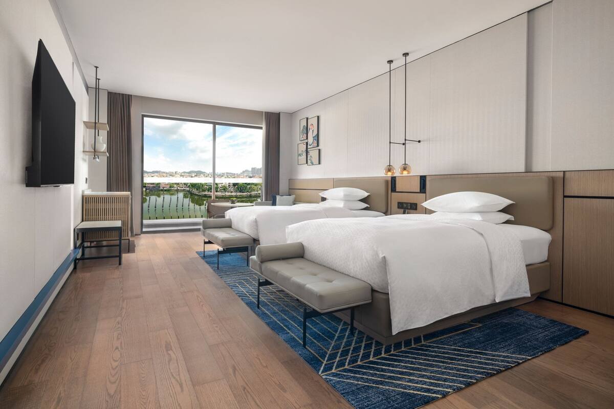 Une chambre d’hôtel moderne dotée d’un grand lit, d’un lit plus petit, d’un coin salon et offrant une vue sur la ville.