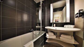 A modern bathroom with dark tiled walls, a glass-enclosed shower, a white sink, and a large mirror.