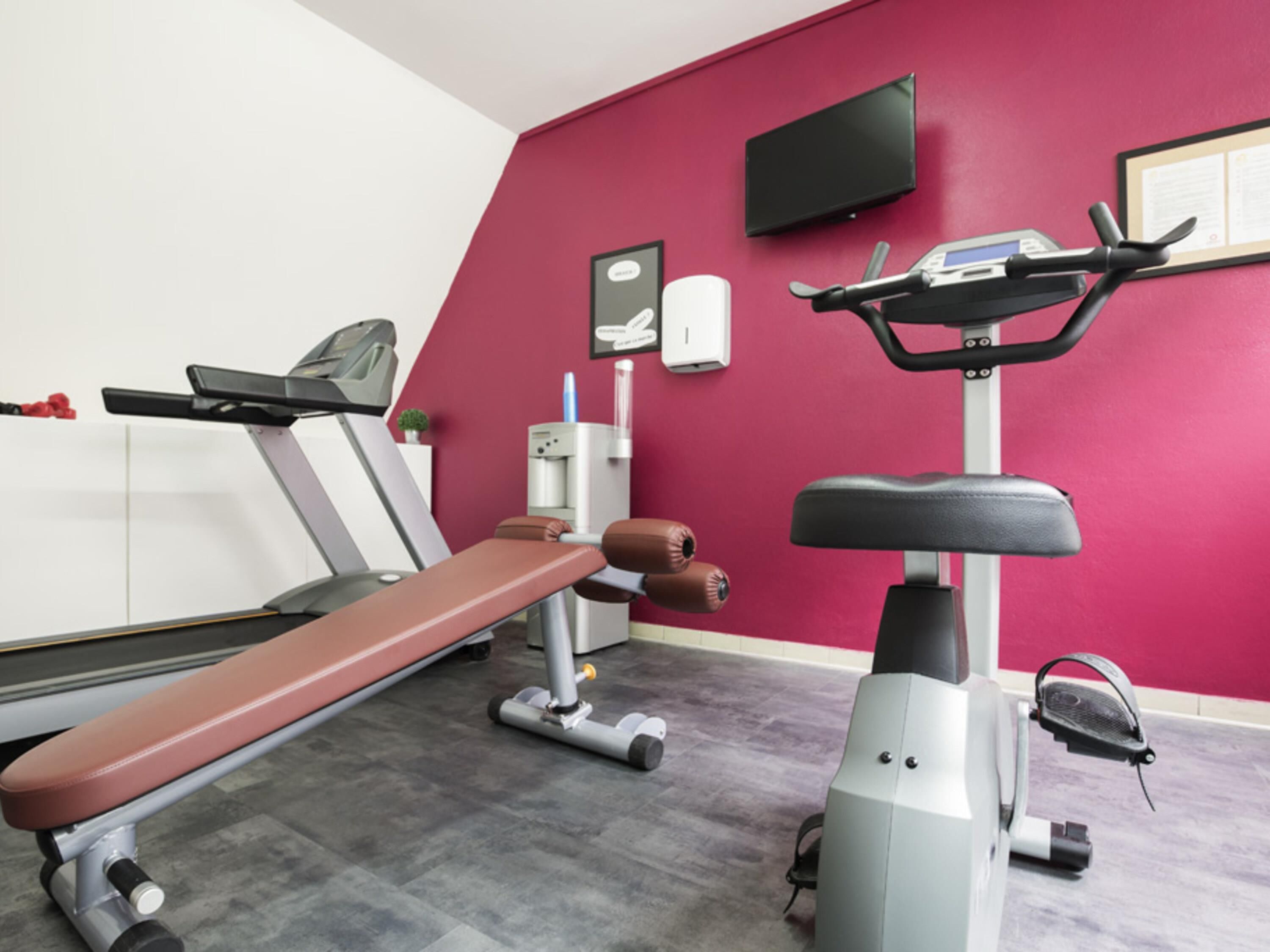 A gym with exercise equipment, a bench, a wall-mounted TV, and a water dispenser.
