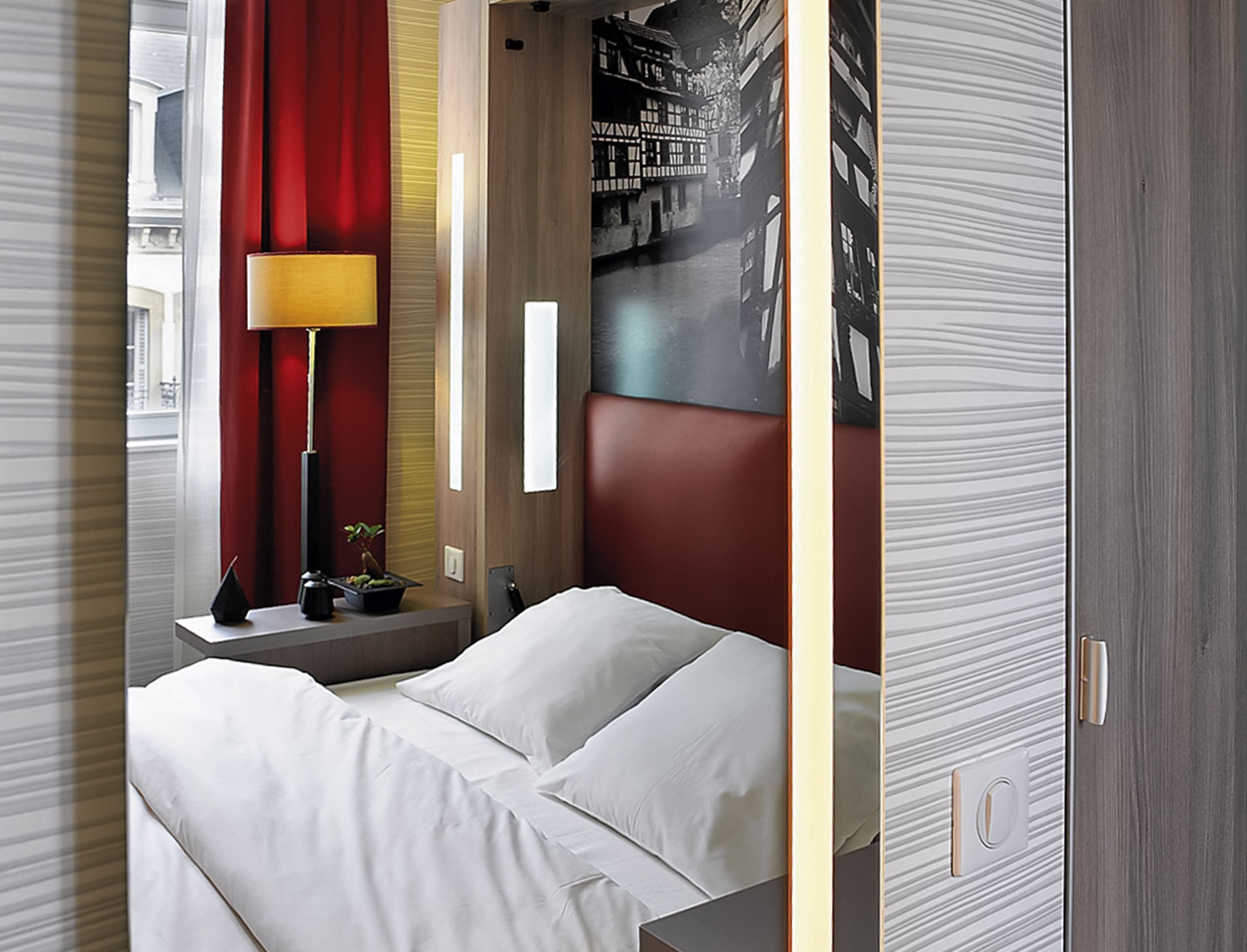 Une chambre d’hôtel comprenant un lit, une table de chevet, une lampe et une œuvre d’art accrochée au mur.