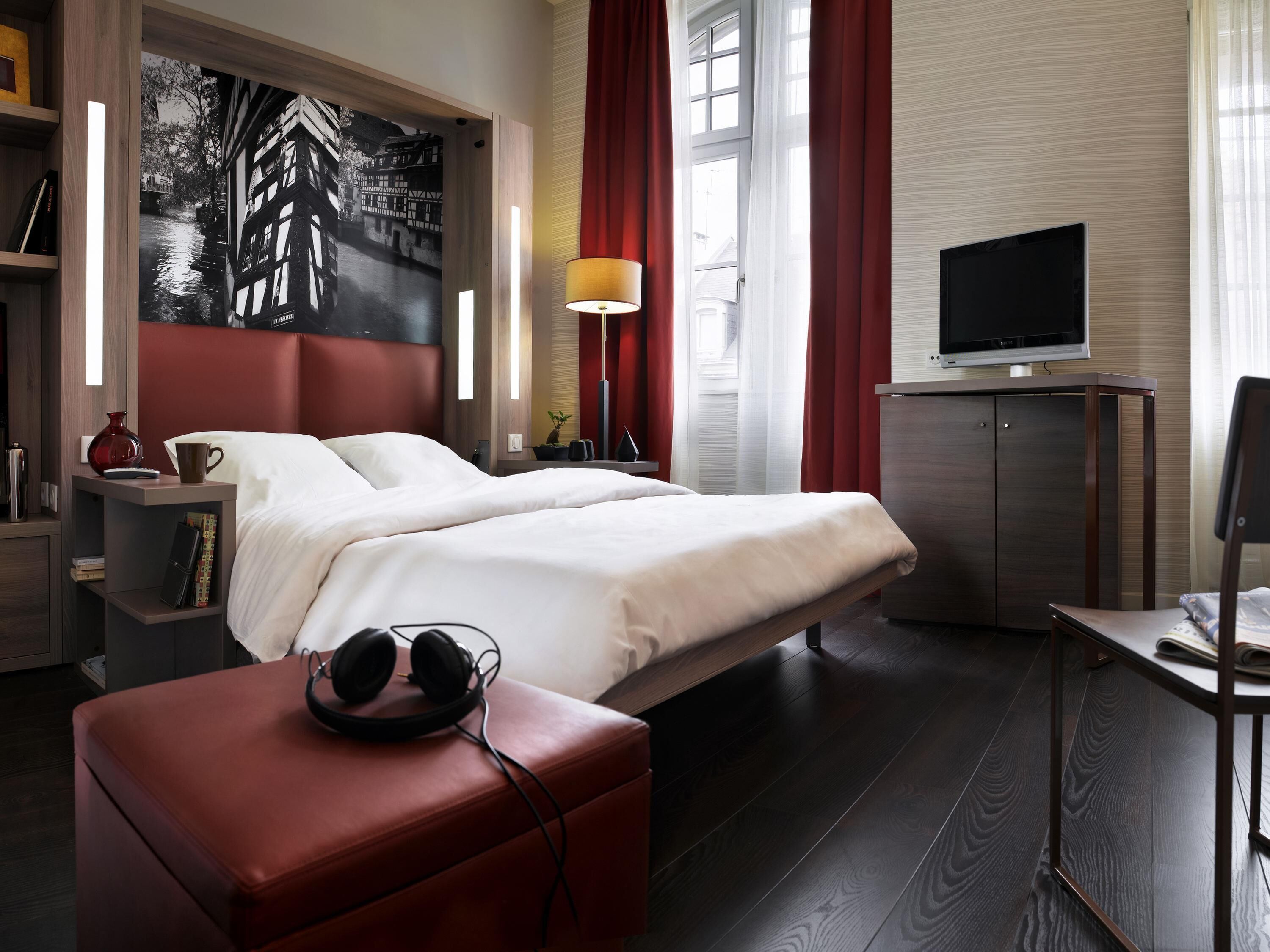 Habitación de hotel moderna con una cama grande, un televisor de pantalla plana, un escritorio con lámpara y un cuadro en la pared.