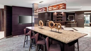 Una cocina moderna con encimera de granito, taburetes de bar, televisor de pantalla plana y horno empotrado.