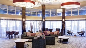 Un hall espacioso con techo alto, ventanas grandes y muebles modernos, incluyendo sofás, sillas y una mesa redonda.