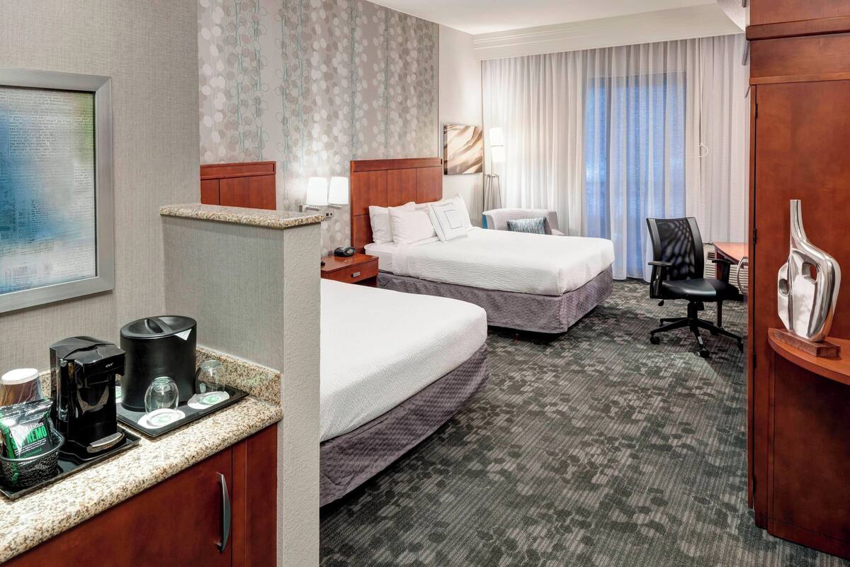 Een hotelkamer met twee bedden, een bureau, een stoel, een koffiezetapparaat en een televisie.