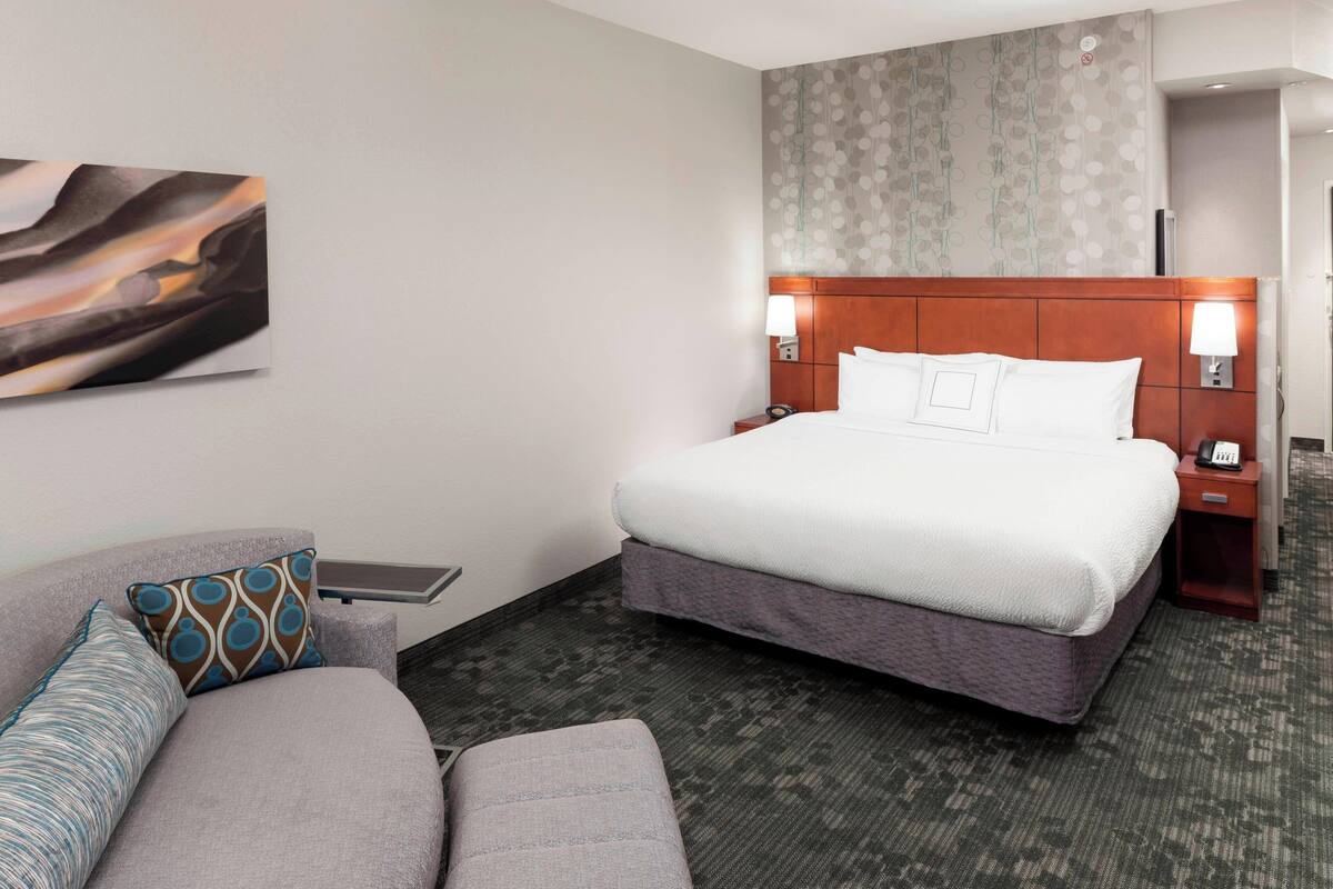 Een hotelkamer met een groot bed, een slaapbank, een nachtkastje met een lamp en een kunstwerk aan de muur.